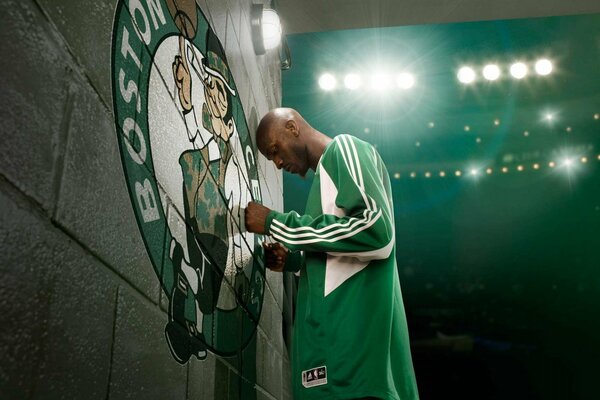 Basketbrlrst in a green uniform prays in front of the club s emblem