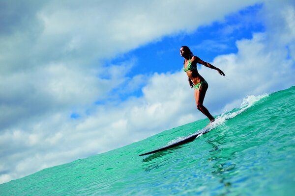 Surfista ragazza rotola sull acqua su uno sfondo di nuvole