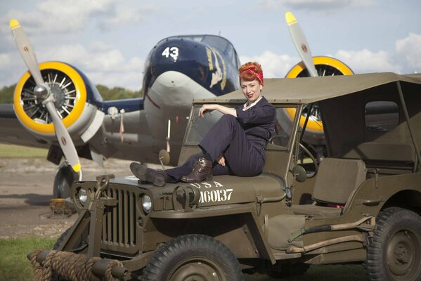 A girl in a blue jumpsuit is sitting in a military car