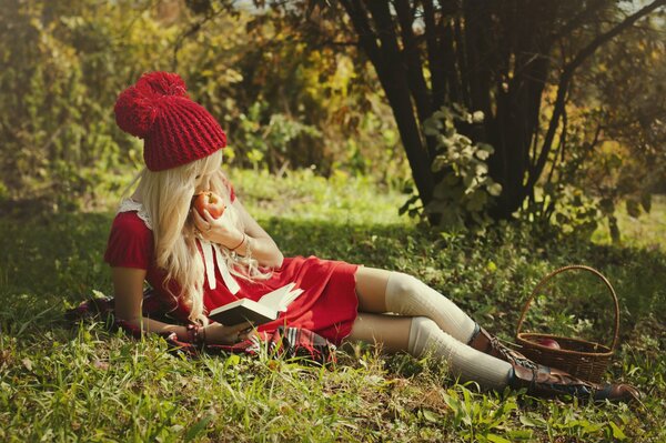 A girl in a red hat eats an apple in the forest