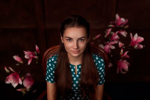 Fille dans une robe à pois assis dans une chaise sur un fond de fleurs