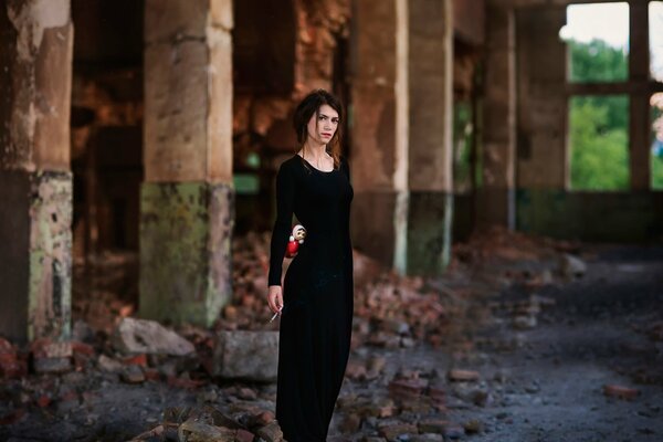 A girl in a black dress with brown hair with a kettlebell in her hands against the background of an abandoned building