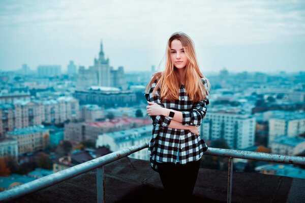 Девушка в клетчатой рубашке на фоне города