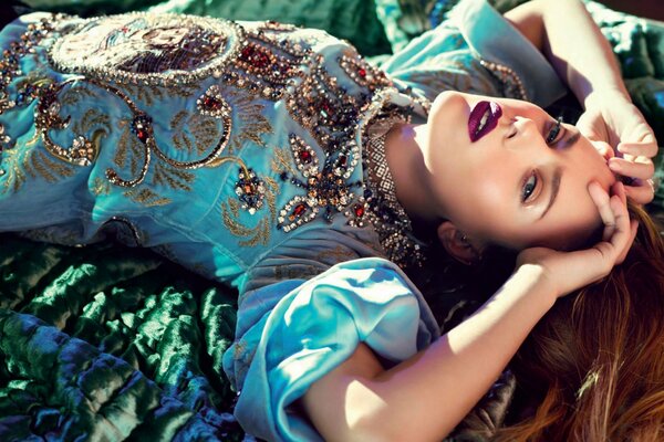 La jeune fille aux cheveux roux et aux lèvres violettes se trouve dans une ancienne robe bleue russe sur un tissu vert