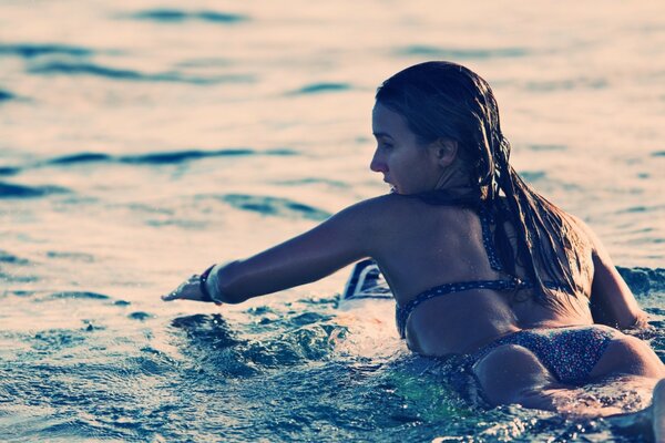 A girl in a bikini is floating on a surfboard