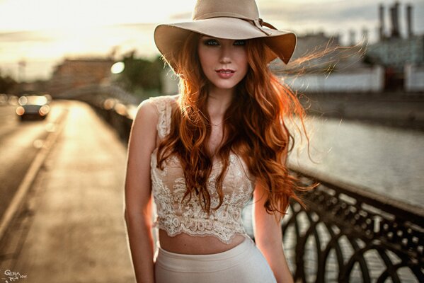 Bellezza rossa con cappello che cammina sul ponte