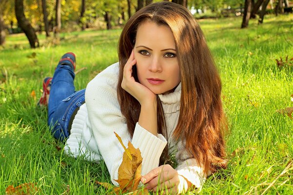 Hermosa chica con el pelo largo yace en la hierba en el otoño