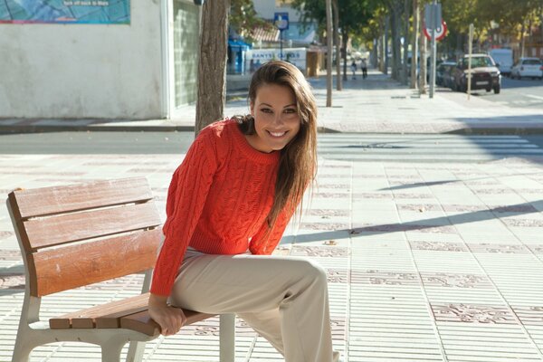 The girl is happy on the bench with a red sweater