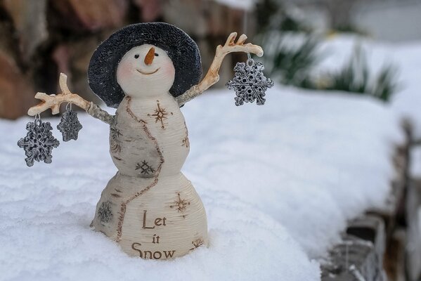 Un pequeño muñeco de nieve sonriente con un sombrero sostiene juguetes de copos de nieve