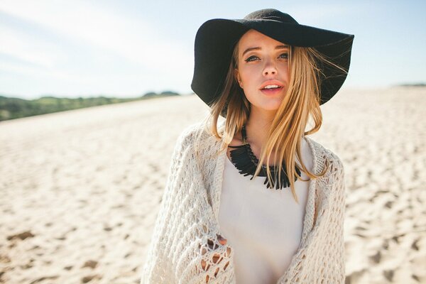 A girl in a black hat on a background of white sand