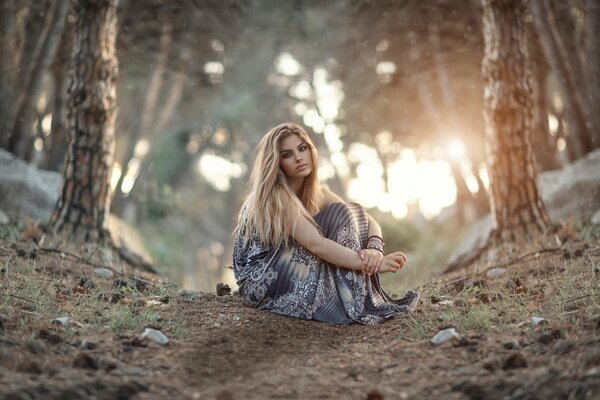 Mädchen sitzt im Wald vor dem Hintergrund des Sonnenuntergangs der Sonne