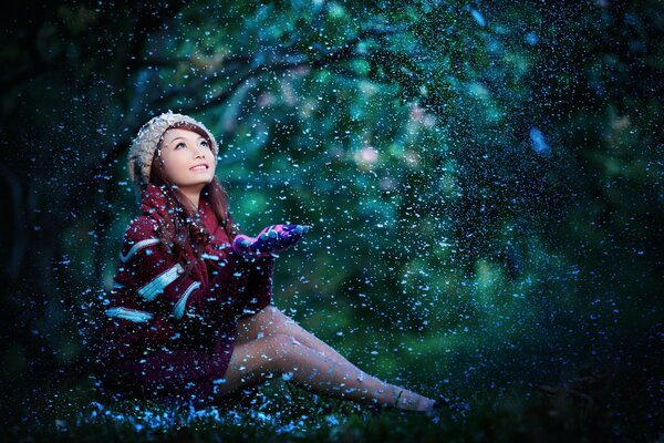 A girl with an Asian appearance catches snowflakes with her palms