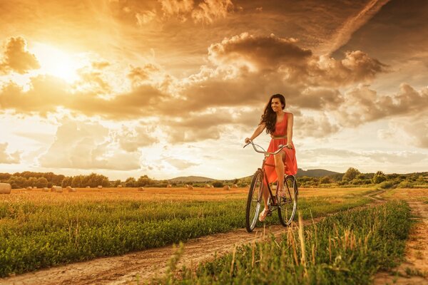 A girl rides a bike on the road at sunset