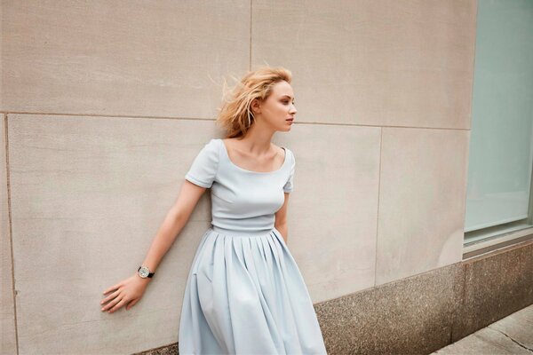 A model girl in a white dress poses against a wall