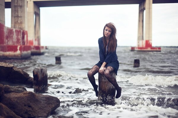 The brunette is sitting on a pole by the sea