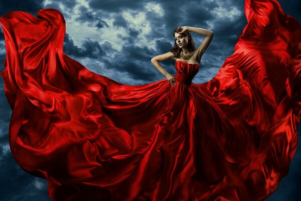 A girl in a red long dress against a gloomy sky