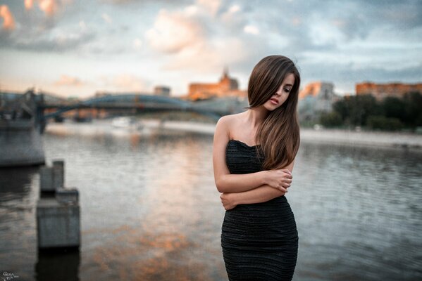 Ekaterina Uspenskaya. Mädchen im schwarzen Kleid auf der Wasserbrücke am Fluss