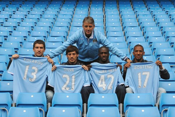 Four men in the stands are holding blue T-shirts in their hands, another man is standing over them