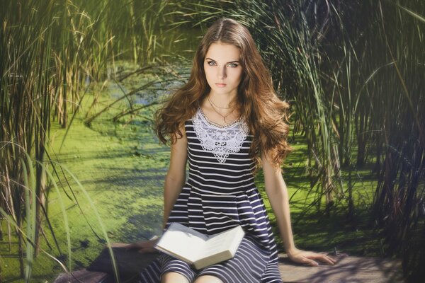 Chica de pelo oscuro se sienta en cañas con un libro