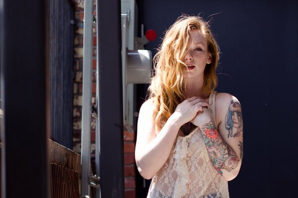 A red-haired girl with freckles and tattoos on her arms
