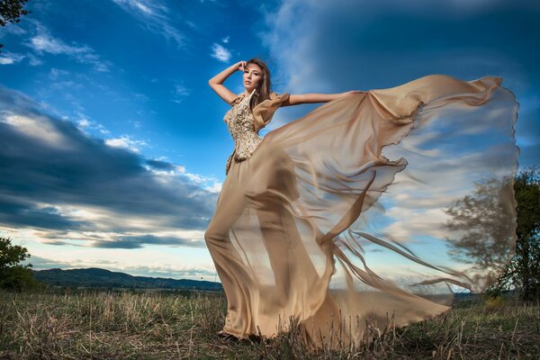 A girl in a beautiful dress poses against the sky