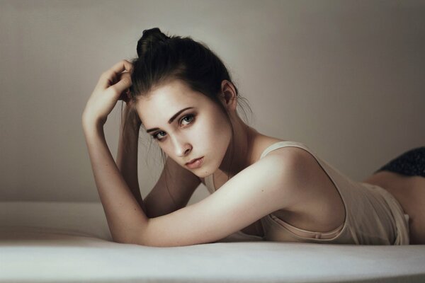 A girl with green eyes and brown hair in a bun is lying on the bed