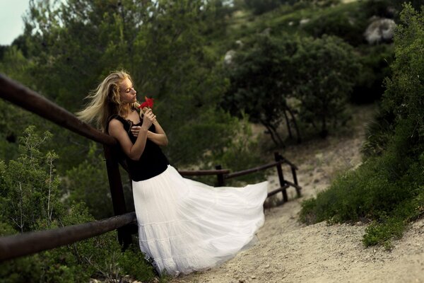 A girl in a white airy skirt with a red flower in her hands