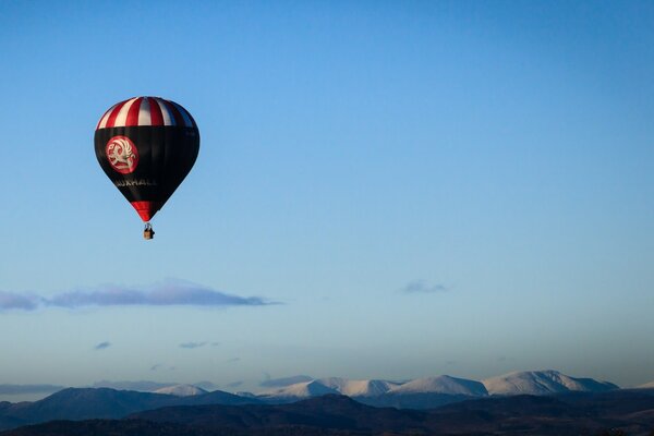 A dark balloon is flying across the sky against the background of mountains