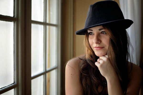 Fille au chapeau regarde par la fenêtre