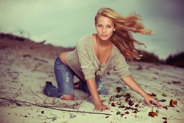 A girl in jeans is photographed on the sand