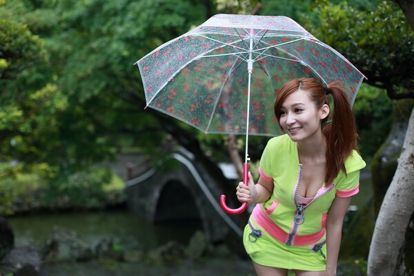 An Asian girl in a light green suit with a cleavage smiles under a transparent umbrella at the bridge