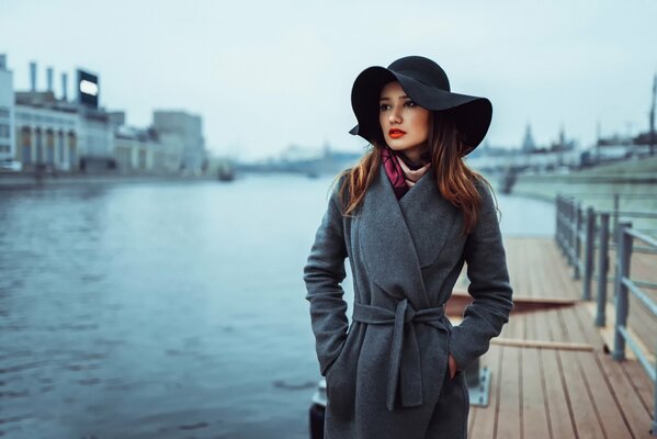 A girl in a black hat and brown hair on the background of the pier