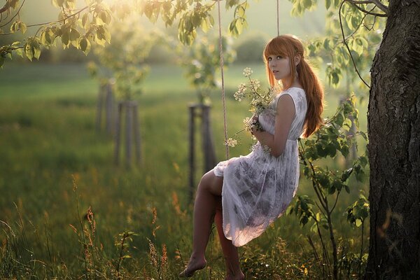 A girl with flowers on a swing under a tree