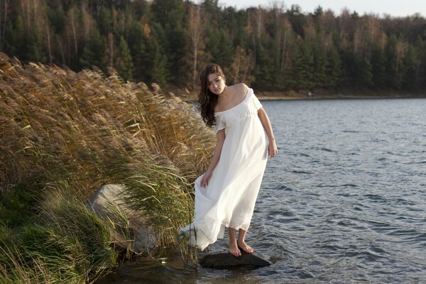 A girl in a white dress fluttering in the wind, on the river bank