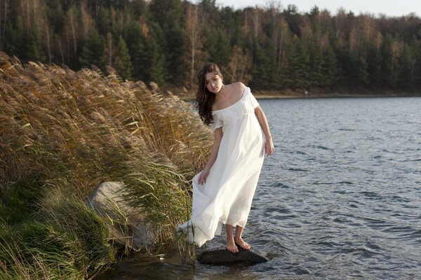 Ragazza in abito bianco svolazzante nel vento, sulla riva del fiume