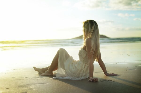 Mädchen im Sommerkleid sitzt auf dem Sand