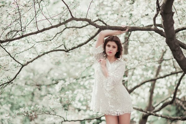 A girl in a white light dress by a flowering tree