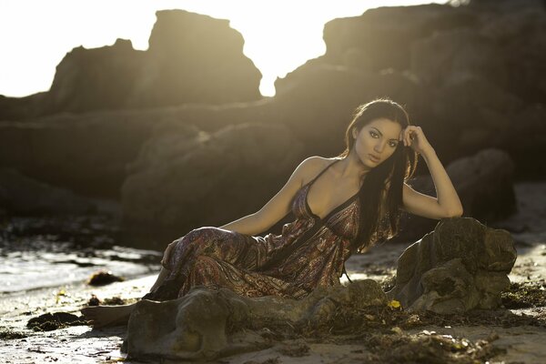 A girl in a dress on the coast by a stone