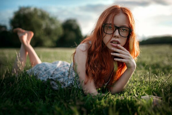 A red-haired girl with glasses is lying on the grass