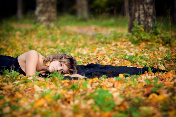 Девушка лежит в листве в осеннем лесу