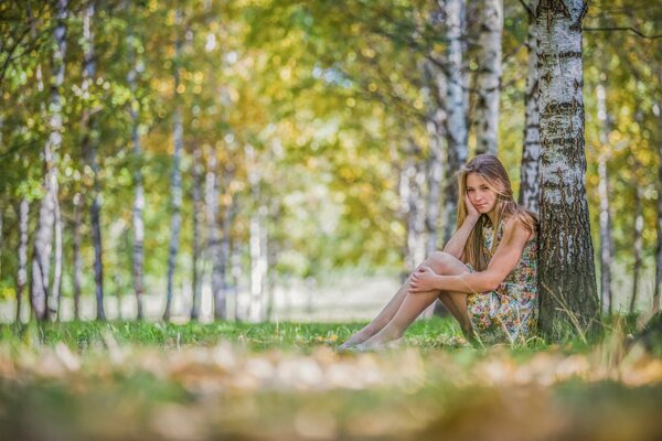 Dziewczyna w sukience siedząca przy drzewie w lesie
