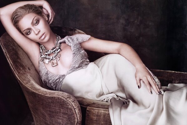 A chic Beyoncé in jewelry is bohemian lying on a chair