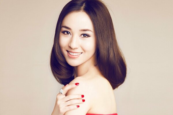 Asian woman with a red manicure on a white wall background