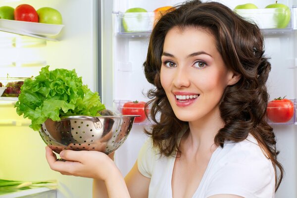 La ragazza al frigorifero tiene una ciotola di insalata