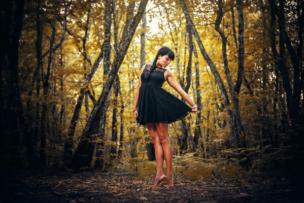 Brunette in a black dress in the autumn forest