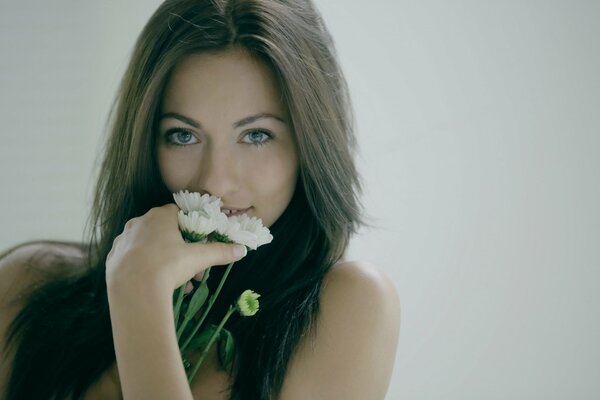 A girl with beautiful blue eyes holds a bouquet of daisies