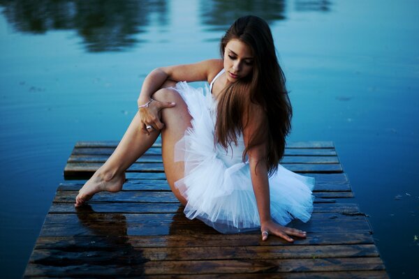 Bailarina chica sentada junto al lago en el muelle