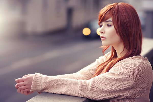 A red-haired girl looks into the distance at the road