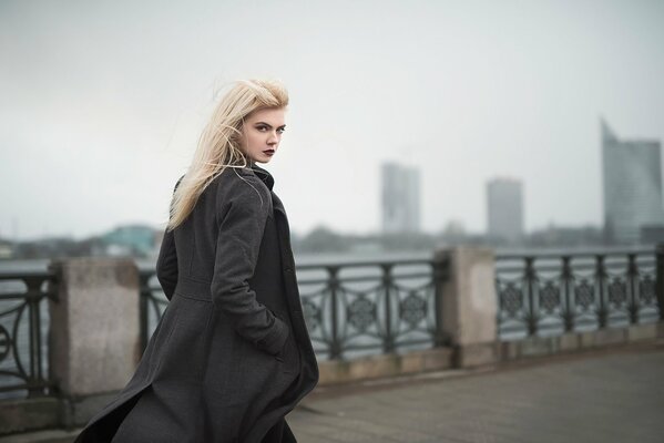 Blonde in a coat walks along the embankment