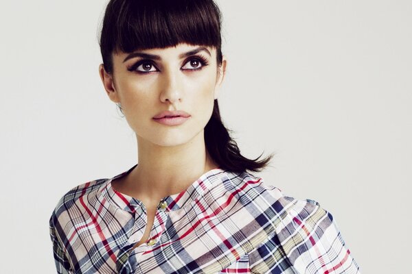 Penelope Cruz in a plaid shirt, with her hair in a ponytail